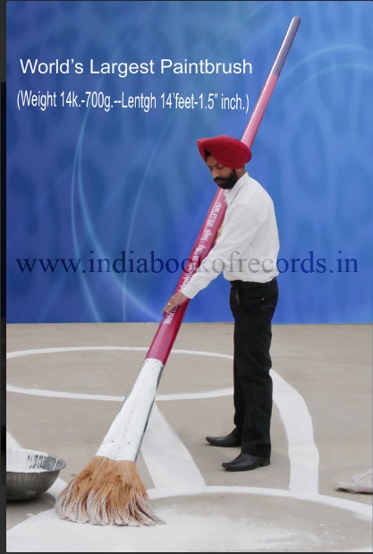 Artist Gurpreet Singh Komal standing beside his record-setting 14-foot paintbrush in Moga, Punjab